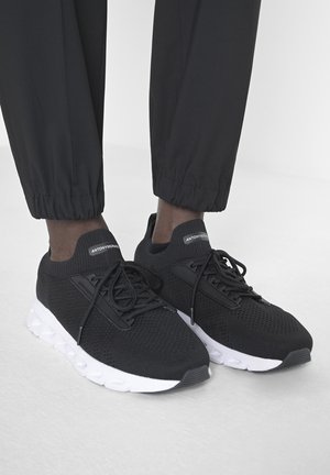 Baskets de sport noires avec tige en maille, détails texturés et semelle en caoutchouc blanche. Comprend des lacets noirs et un logo sur la languette.