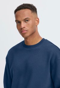 Sudadera azul marino hecha de una tela suave, con cuello redondo y puños acanalados, que presenta un corte relajado y detalles de costura mínimos.