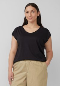 Zwarte T-shirt met korte mouwen en V-hals, gemaakt van zachte stof, gecombineerd met lichtbeige elastische taillebroek. Eenvoudig ontwerp, zonder patronen of hardware.