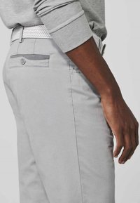 Light gray pants with a smooth texture, featuring a back pocket with a button closure and a woven white belt.