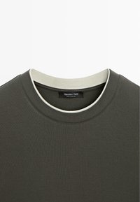 Donkergroene T-shirt met een ronde halslijn, voorzien van een contrasterende lichte accentkleur rond de kraag en een label aan de binnenkant.