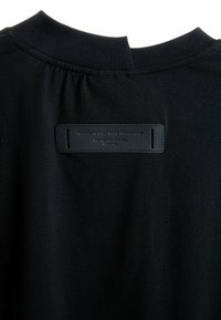 Prenda de tela negra con escote fruncido y etiqueta rectangular cosida que dice "OBF DESIGN AGENCY IN SPAIN" en la parte posterior.