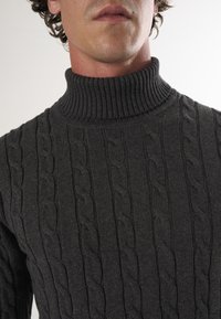 Ciemnoszary sweter z kołnierzem typu golf i wzorem w warkocze. Zbliżenie ukazujące szczegółowe przeszycia i fakturę materiału.