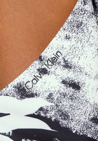 Tessuto a motivi bianco e nero con finitura testurizzata. Presenta un colletto e il logo "Calvin Klein" in nero lungo il bordo.