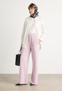 White button-up shirt over a white top, paired with light pink wide-leg sweatpants. Black and white striped scarf and small black handbag.