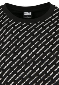 Schwarzes T-Shirt mit Rundhalsausschnitt und diagonaler weißer Schrift "URBAN CLASSICS" sowie einem sichtbar bedruckten Größenetikett im Kragen.