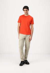 Camiseta de algodón roja con cuello redondo, combinada con pantalones cargo beige claros con bolsillos laterales y zapatos negros con cordones.