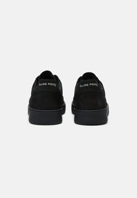 Paire de baskets basses noires avec semelles épaisses, vues de dos, avec le texte blanc "Filling Pieces" sur les languettes de talon.