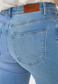 Jeans in denim blu chiaro con vita alta, dotati di un'etichetta in cuoio marrone, due tasche posteriori e dettagli di cucitura classici.