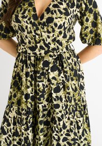 Wrap dress featuring a green and black animal print pattern, short sleeves, a fitted waist with a tie, and a flared skirt. Textured fabric.