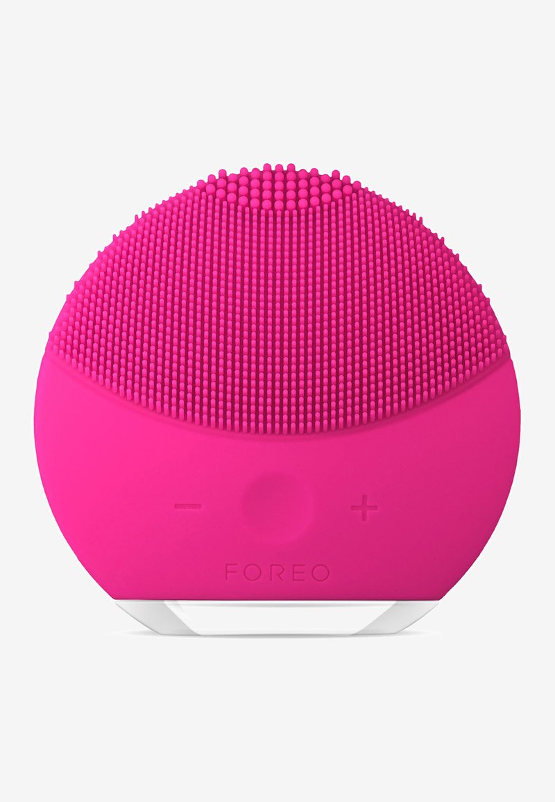 Dispositivo per la pulizia del viso in silicone rosa, di forma ovale con setole in silicone texturizzate sulla parte superiore, pulsanti di controllo più/meno e una base bianca.
