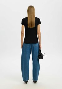 Sort t-shirt med korte ærmer, der er parret med højtaljede, vide blå denimjeans. Afsluttes med sorte højhælede sko og en lille sort taske.