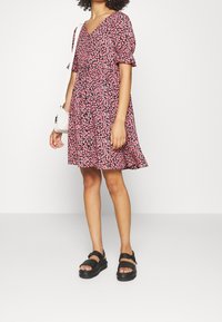 Květinové šaty s krátkými rukávy, véčkovým výstřihem, růžovými květy na černé látce, rozšířené lemy. V kombinaci s černými sandály a bílou kabelkou.