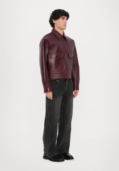 Burgunderfarbene Kunstlederjacke mit zwei Brusttaschen und Reißverschluss vorne, kombiniert mit schwarzen weit geschnittenen Jeans mit seitlichen Nahtdetails.