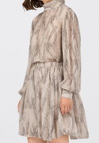 Abito beige con motivo di punti neri astratti, collo alto, lunghe maniche a sbuffo e vita elastica, realizzato in tessuto leggero e trasparente.