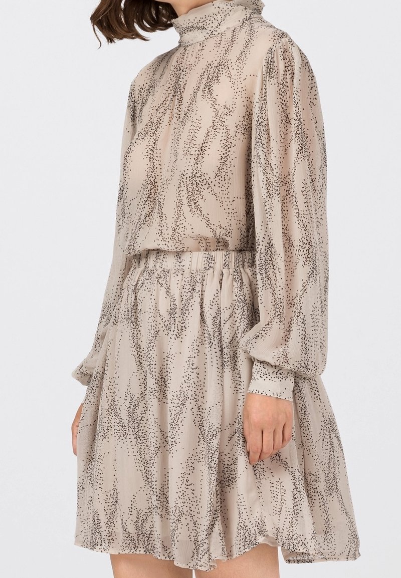 Abito beige con motivo di punti neri astratti, collo alto, lunghe maniche a sbuffo e vita elastica, realizzato in tessuto leggero e trasparente.
