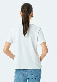 Weißes Baumwoll-T-Shirt mit kurzen Ärmeln, rundem Kragen und lässiger Passform, kombiniert mit hoch taillierten blauen Jeans.