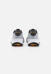Sneaker in rete grigia con accenti neri, dotate di una suola bianca e dettagli gialli. Il design include un'etichetta di presa sul tallone.