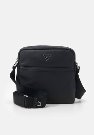 Zwarte rechthoekige crossbodytas met verstelbare riem, voorvak met ritssluiting en een zilveren driehoekig Guess-logo in het midden.