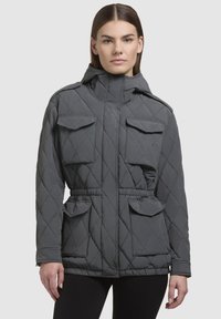 Siva jakna s podstavom, dijamantnim quilted uzorkom, visokim ovratnikom, dvadžepna džepa i pojasom na izvlačenje. Glatka, mat tekstura.