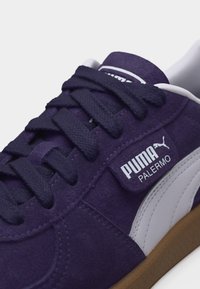 Μωβ παπούτσι Puma Palermo από σουέντ με μαύρα κορδόνια, λευκή πλευρική ρίγα και καφέ σόλα, που εμφανίζει το λογότυπο Puma στο πλάι.