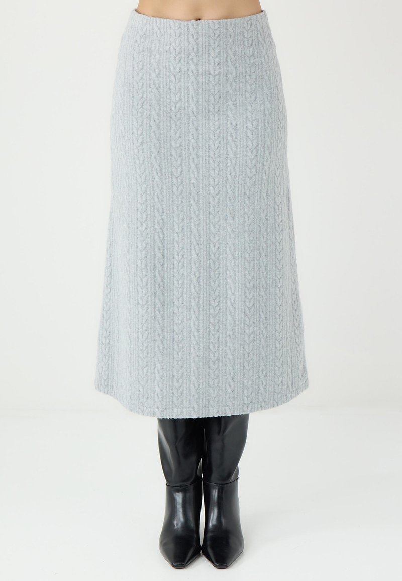 Jupe midi tricotée gris clair avec une texture côtelée et un motif de feuilles, complétée par des bottes noires à bout pointu.