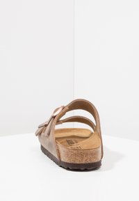 Brun sandal med en metallisk rosa accent på remmen, korksula, öppen baksida och strukturerad gummisula för bra grepp.