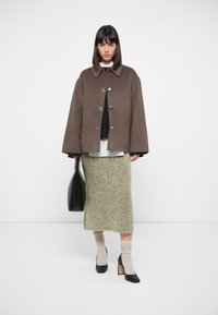 Brown wool-blend cropped jacket with a rounded collar and snap buttons, paired with a green textured skirt, black heels, and a black bag.