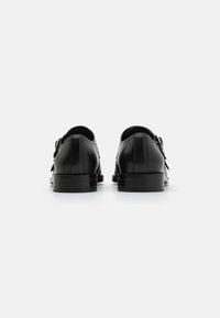 Black leather shoes with a smooth finish, rounded toe, and flat soles. Features an adjustable strap and minimalistic design.