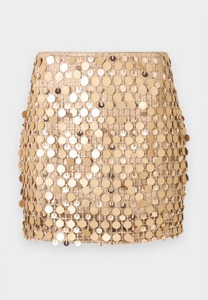 Μίνι φούστα με παγιέτες σε χρυσό χρώμα, διακοσμημένη με στρογγυλά μεταλλικά δίσκακια ραμμένα πάνω σε δίχτυ, δημιουργώντας μια αντανακλαστική, υφή επιφάνεια.