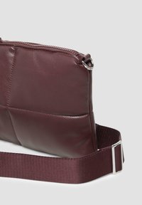 Burgunderfarbene Lederhandtasche mit strukturiertem Oberflächen, rechteckiger Form, Reißverschluss und einem Stoffgurt mit einer Metall-Schnalle.