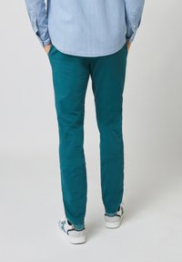 Pantalones de algodón en color teal con corte slim, que cuentan con bolsillos laterales, y combinados con zapatillas blancas que tienen un patrón de acento azul.