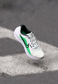 White athletic shoe with green accents, black swoosh, lightweight mesh upper, lace closure, padded collar, and white sole.