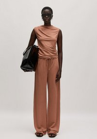 Sandy brown twee-delige outfit met een gedrapeerde top en wijde broek, gemaakt van zachte stof. Zwarte oversized handtas en zonnebril.