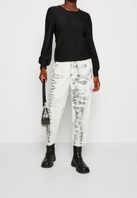 Top nero a maniche lunghe con texture e polsini elasticizzati, abbinato a jeans bianchi a vita alta con motivo tie-dye nero. Stivaletti neri alla caviglia.