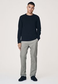 Camicia nera a maniche lunghe, pantaloni grigio chiaro e scarpe nere. Design semplice, vestibilità standard, colori solidi, senza motivi o loghi visibili.