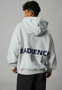 Felpa grigia con una grande stampa blu navy con la scritta "RADIENCE" sul retro, presenta un cappuccio con cordino e polsini e orlo a costine.