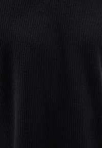 Svart ribbat tyg med en strukturerad yta som visar vertikala linjer och en mjuk, stickad look. Inga synliga knäppningar eller detaljer.