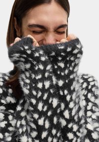 Schwarzer und weiß gepunkteter, flauschiger Pullover mit hohem Kragen und langen Ärmeln, der ein strukturiertes, weiches Materialdesign aufweist.