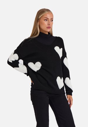 Black knit sweater with white heart patterns on sleeves, wide neckline, and relaxed fit, paired with black pants. Textured fabric.