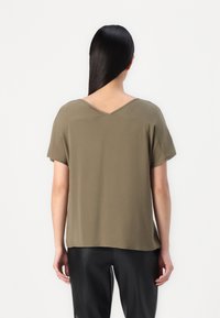 Haut à manches courtes vert olive avec un design à dos en V. Tissu doux avec une coupe décontractée, présentant des bords légèrement roulés et un ourlet droit.