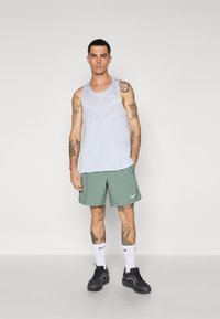 Hellblaues Tanktop mit Meshstruktur und weißem Nike-Logo, kombiniert mit grünen Shorts und schwarzen Sportschuhen. Weiße Sportsocken getragen.