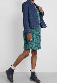Dark denim jacket with a collar, paired with a green patterned dress featuring white floral accents. Black ankle boots with textured socks.