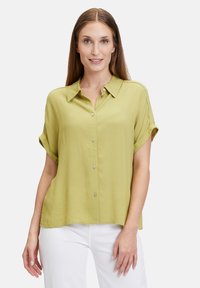Short-sleeve, button-up shirt in light green fabric with a smooth texture and a collar. Features rolled sleeves and subtle side slits.