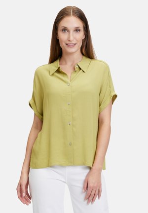 Short-sleeve, button-up shirt in light green fabric with a smooth texture and a collar. Features rolled sleeves and subtle side slits.