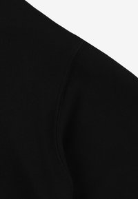 Czarna faktura materiału pokazująca szew na ramieniu, podkreślająca miękkość i grubość materiału. Brak dodatkowych obiektów lub kontekstu.