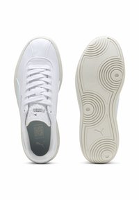 Et par hvide Puma sneakers, venstre sko set fra oven med snørebånd og logo, højre sko sål med cirkulært mønster og Puma-logo.