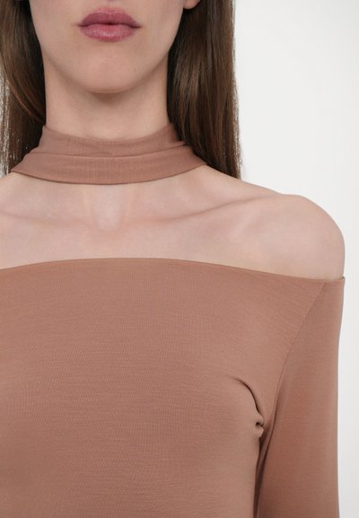 Pruun õlavarrelt avatud topp kõrge ja sobiva kaeluse ning sujuva ja soonilise materjaliga, mis näitab sleek siluetti ja peent tekstuuri.