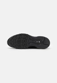 Semelle extérieure en caoutchouc noir d'une sneaker avec des motifs de semelle et un logo Nike blanc visible dans la zone du talon.