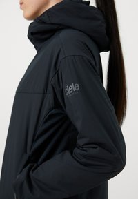 Črna atletska jakna s kapuco, ki se ponaša s sleek dizajnom, gladko teksturo in logotipom na levem rokavu. Brez vidne strojne obdelave ali vzorcev.